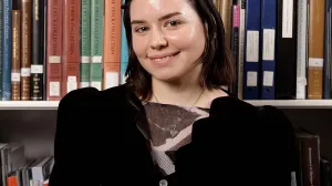 A woman with short brown hair smiling in front of shelves filled with books