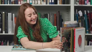 Woman in a green shirt picking a book from a stack of books on a table