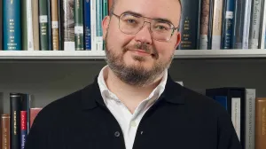 Man in a black cardigan in front of a bookshelf