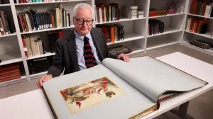 video still of Stephen Bury with large book with print open 