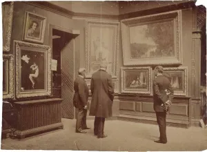 Three men in long coats viewing framed paintings hanging on a wall