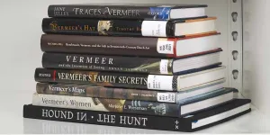 Stack of eight books about Vermeer on a white shelf