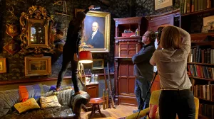 A photographer taking a photo of a portrait in a richly decorated room, with two others assisting.