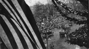 A military parade along Fifth Avenue, with an American flag and leafy garlands in the foreground