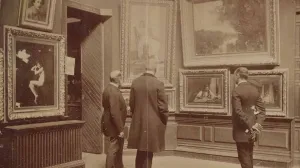 Three men in long coats viewing framed paintings hanging on a wall