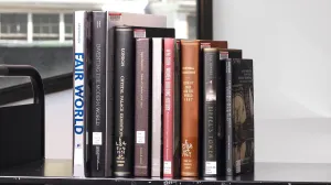 Nine books stacked vertically on a library cart in front of a window