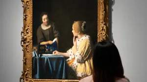 Woman looking at a painting of a female maid handing a letter to a seated woman in a yellow coat