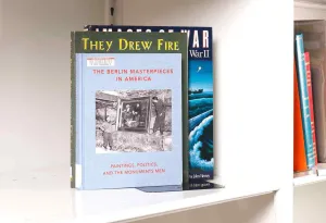 Three books stacked on a white shelf. The front book cover features an image of two soldiers recovering an oil painting.