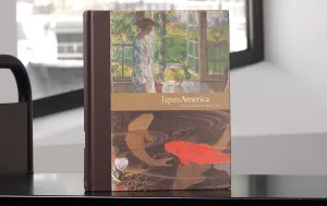 Book with details of a Japanese-inspired Western painting and a Japanese artwork of fishes on its cover on a library cart in front of a window