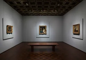 Gallery with gray walls in which three gold-framed photos hang