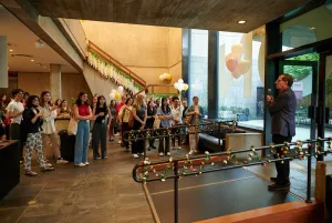 Man on a microphone speaking to standing guests in a lobby decorated with flowers