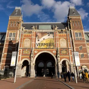 Exterior of a museum with a large poster with the word Vermeer and a close-up of a woman with a pearl earring wearing a fur-trimmed yellow coat