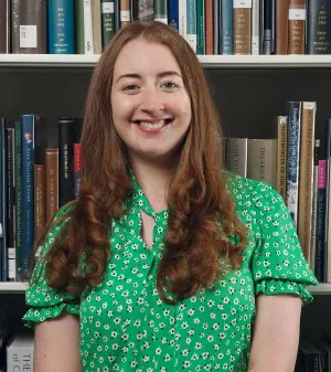 Woman in a green shirt smiling in front of a bookshelf