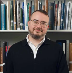 Man in a black cardigan smiling in front of a bookshelf