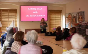 Woman presenting to a classroom of elderly people in front of a screen reading