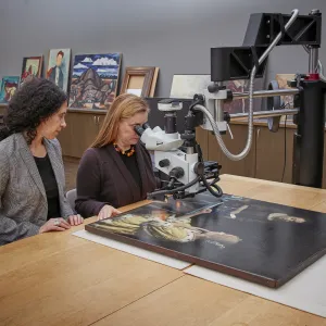 Two conservators seated at a table in a lab, one looking at Vermeer's