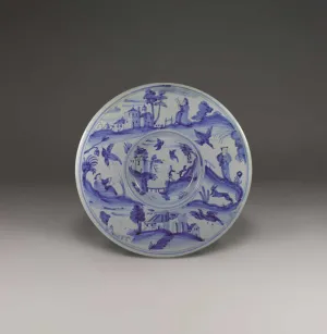 Earthenware plate in blue and white with a landscape scene of a figure and dog walking uphill at the center and more landscape scenes of figures and animals on the outside.