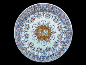 Earthenware platter with four nude figures in the middle surrounded by floral designs in blue and orange