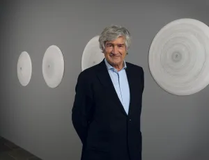 Man in suit in front of four porcelain disks on a grey wall